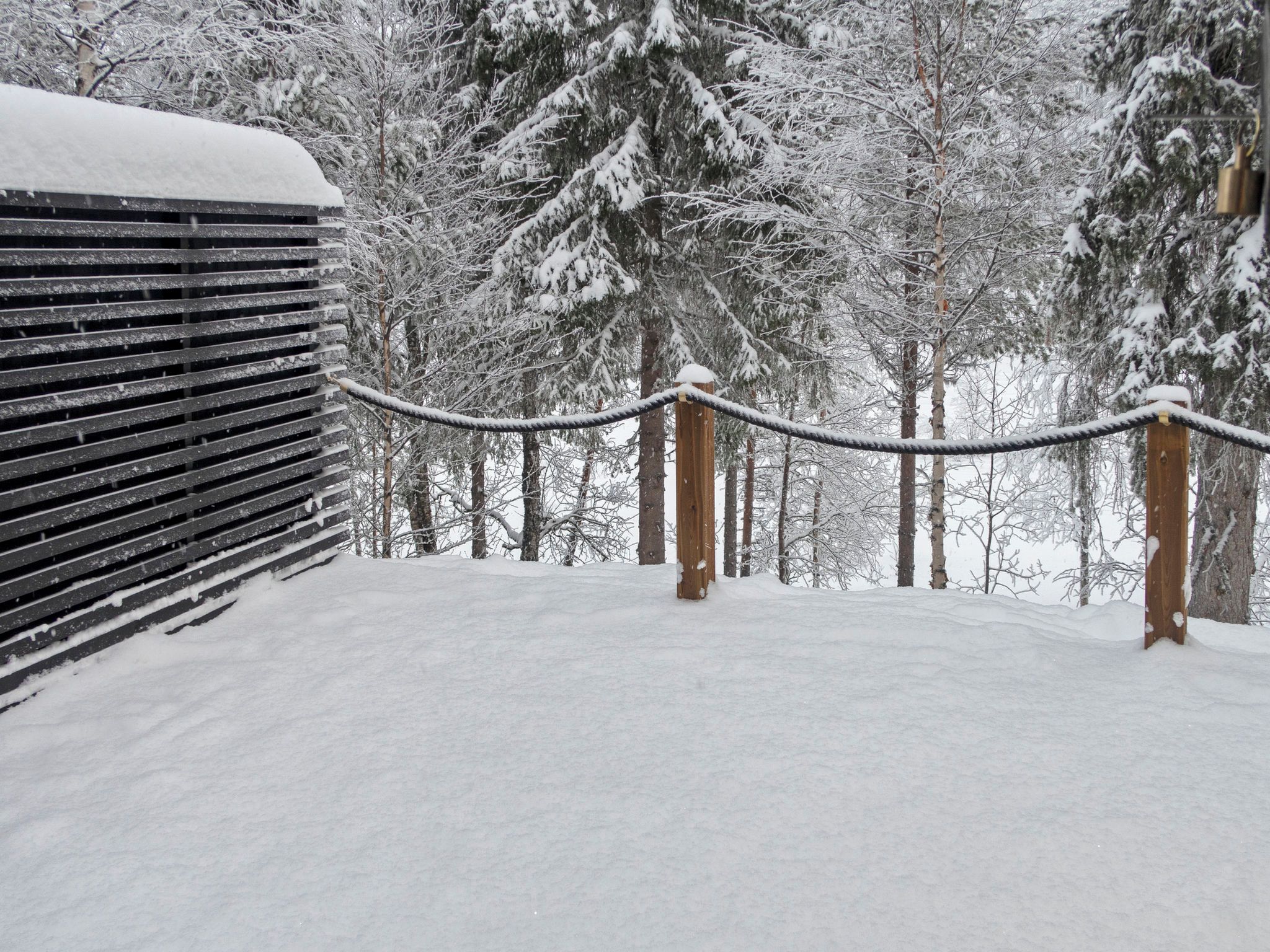 A snow-covered outdoor area with a wooden fence and a rope barrier.