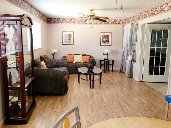 A living room with a sofa, two lamps, a ceiling fan, and a door leading outside.