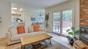 A living room with a sofa, coffee table, and fireplace. There is a kitchen in the background and a sliding glass door leading to a deck.