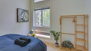 A bedroom with a bed, a window, a wooden shelf, and a potted plant.