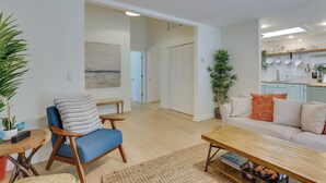 A modern living room with a blue sofa, wooden coffee table, and a kitchen area with white cabinets and a countertop.