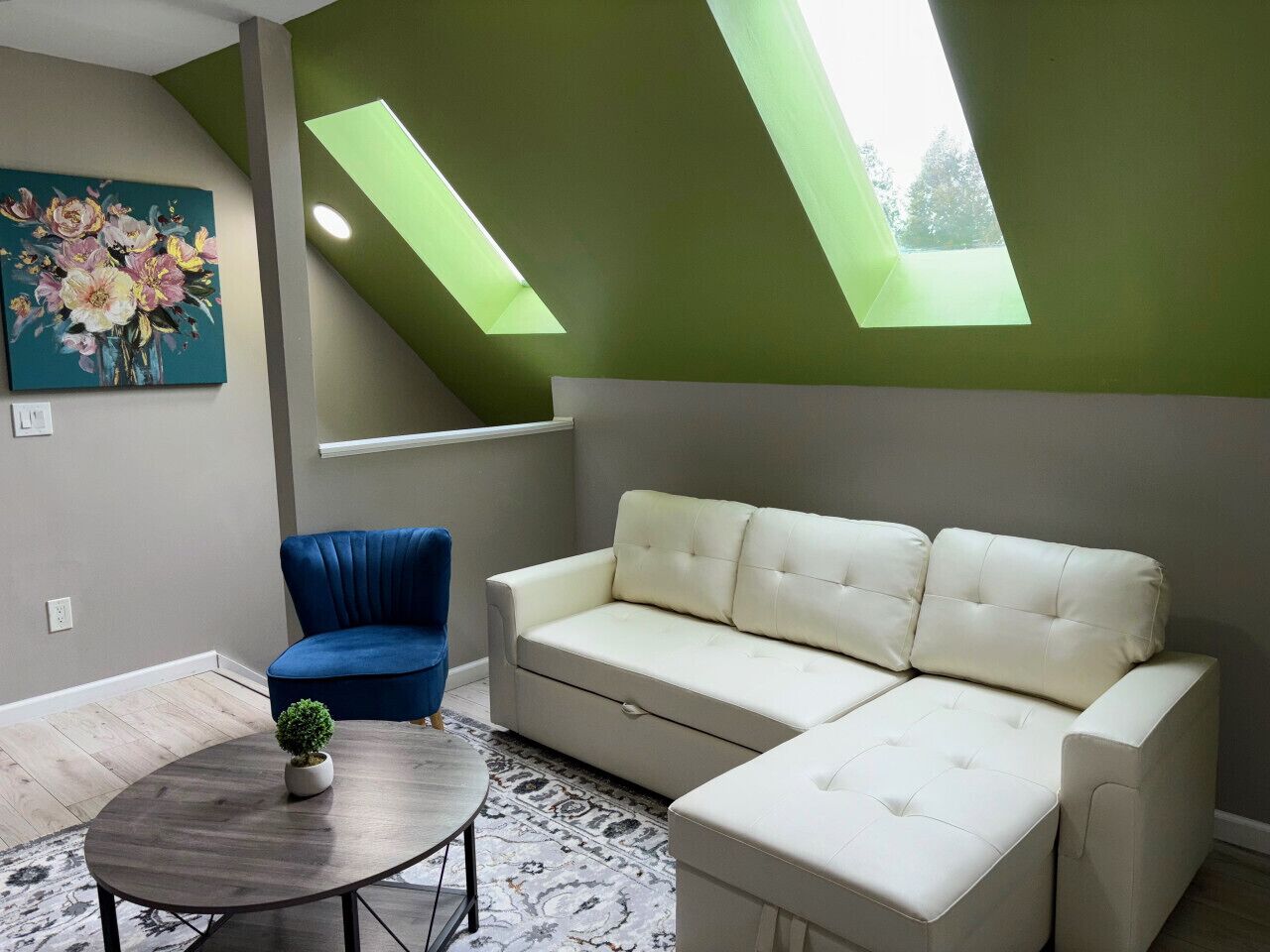 Une pièce avec un canapé blanc, une chaise bleue, une petite table sur laquelle se trouve une plante, et un tableau accroché au mur.