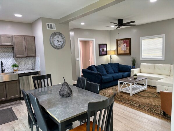 Uma sala de estar moderna com um sofá azul escuro, um sofá branco e uma área de jantar com mesa e cadeiras.