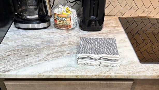 A kitchen with a marble countertop, a coffee maker, a kettle, and a drawer with cooking utensils.