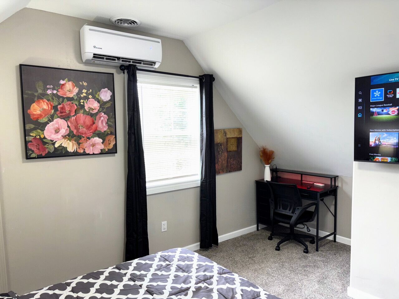 Une chambre à coucher comprenant un lit, un bureau, un climatiseur, une télévision et une fenêtre avec des rideaux.