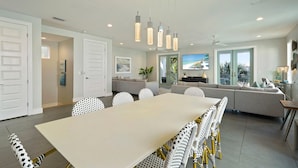 A modern kitchen with a large dining table, white chairs, pendant lights, and a view of the outdoors. - White Pearl - Modern Vacation Rental House in Destiny by the Sea with Shared Pool (Destin)