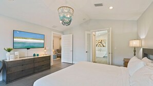 A bedroom with a large bed, a dresser, a television, and a chandelier. - White Pearl - Modern Vacation Rental House in Destiny by the Sea with Shared Pool (Destin)