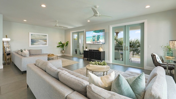 A spacious living room with a large grey sectional sofa, a flat-screen TV mounted on the wall, and a ceiling fan. - White Pearl - Modern Vacation Rental House in Destiny by the Sea with Shared Pool (Destin)