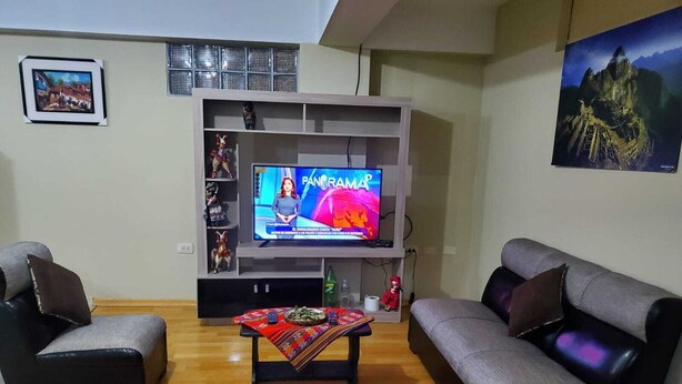 Een woonkamer met twee grijze banken, een salontafel, een tv op een dressoir en een plank met decoratieve objecten.