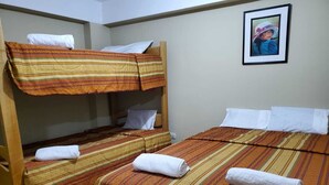 Een kamer met twee eenpersoonsbedden en een stapelbed, elk met gestreept beddengoed en witte kussens.