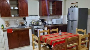 Een keuken met houten kastjes, een eettafel met stoelen, een koelkast en een magnetron.