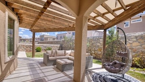 An outdoor patio area with a covered seating area, stone walls, and a hanging chair. - Casa Del Arbol Outdoor Oasis (El Paso)