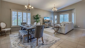 A spacious living room with a dining area, large windows, and a chandelier. - Casa Del Arbol Outdoor Oasis (El Paso)