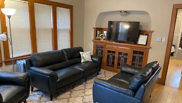 A living room with a black leather sofa, a blue armchair, and a television on a wooden cabinet.