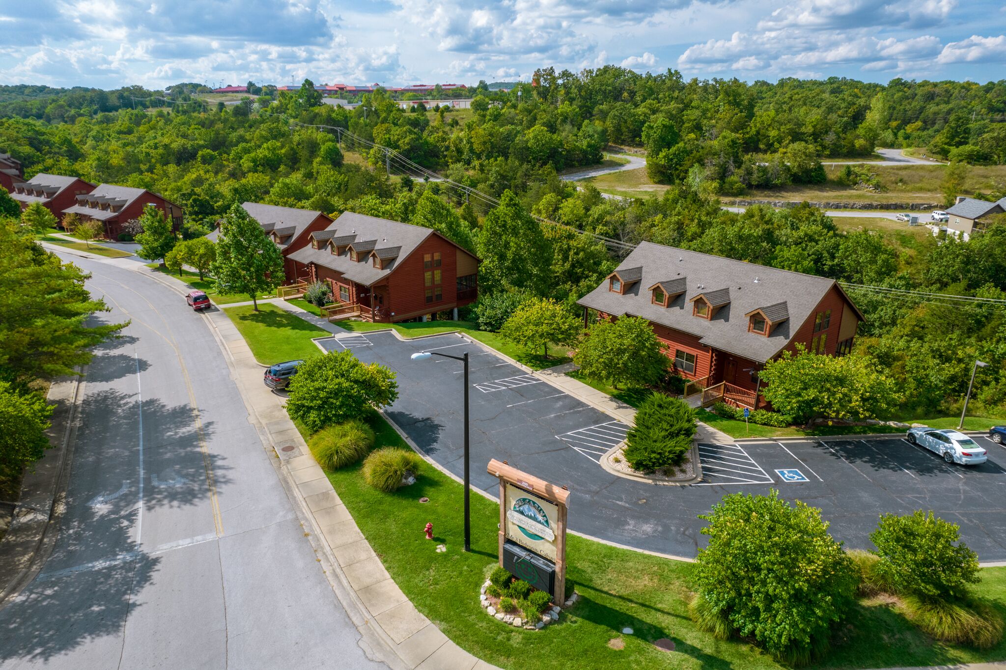 Uma área residencial com várias casas de telhado vermelho, um estacionamento e uma placa indicando um empreendimento habitacional ou conjunto residencial.