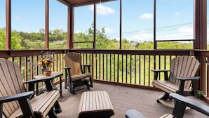 A covered outdoor seating area with wooden chairs and a table, overlooking a lush green landscape. - Relaxing Walk-in Cabin in Branson Theatre District, Golf and Ticket Discounts (Branson)