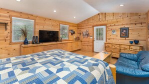 A cozy room with wooden walls, a large bed with a patterned quilt, a television, and a blue leather sofa. - The REAL BOISE RETREAT! AMAZING LOCATION & STELLAR Backyard. Bring your DOG! 2 mins to Downtown! (Boise)