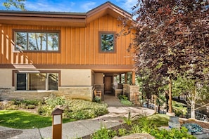 A two-story house with a stone foundation, a wooden exterior, and a landscaped front yard with a pathway leading to the entrance.
