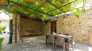 Une terrasse extérieure avec des murs en pierre, des meubles en osier et une pergola recouverte de plantes grimpantes.