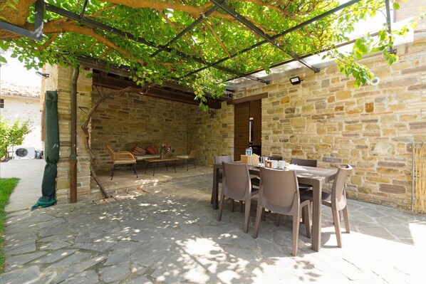 An outdoor patio with stone walls, wicker furniture, and a pergola covered with green vines.