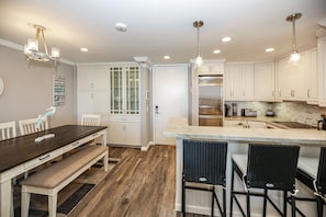 A modern kitchen with white cabinets, a central island, and a dining area with a bench and chairs.