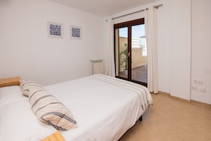Une chambre à coucher comprenant un lit, un radiateur, une porte donnant sur un espace extérieur et deux tableaux encadrés accrochés au mur.