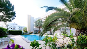 A pool area with lounge chairs, palm trees, and a building in the background. - Apartment Drac Blanc 1-4 close to the Beach with Sea View, Pool, Terrace & Wi-Fi (CALA RATJADA)