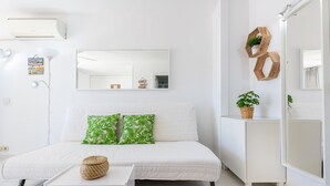 En vit soffa med gröna kuddar, ett litet bord, en spegel och hexagonformad träinredning.