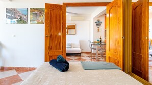 Hotelkamer met een bed, een bureau met stoel en uitzicht op het strand door de open deur.