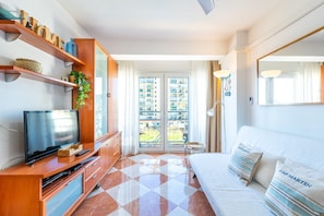 Een moderne hotelkamer met een televisie, houten planken, een bed met gestreepte kussens en uitzicht op een gebouw door het raam.