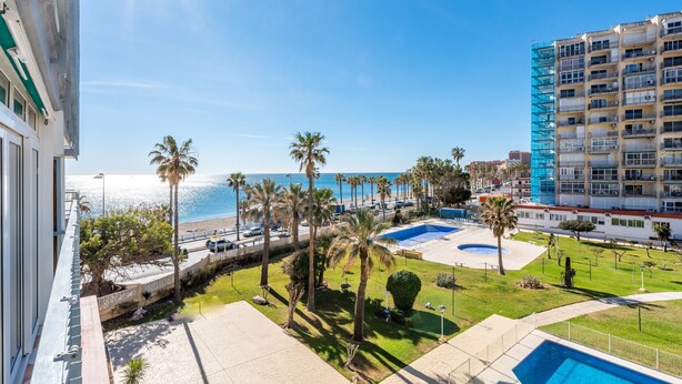 Een hotel met een zwembad, palmbomen en uitzicht op zee.