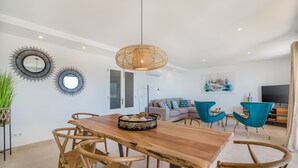 A modern living room with a wooden dining table, wicker chairs, a rattan pendant light, and a sofa with teal chairs. - Stunning Apartment "Cana Ferrera" with Sea and Mountain Views, Balcony, A/C & Wi-Fi (Puerto de Pollensa)