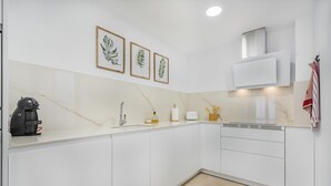 A modern kitchen with white cabinets, a marble countertop, a coffee machine, a sink, and framed botanical prints on the wall. - Stunning Apartment "Cana Ferrera" with Sea and Mountain Views, Balcony, A/C & Wi-Fi (Puerto de Pollensa)