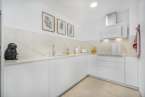 Eine moderne Küche mit weißen Schränken, einer Marmorarbeitsplatte, einer Kaffeemaschine, einem Spülbecken und gerahmten Pflanzenbildern an der Wand.
