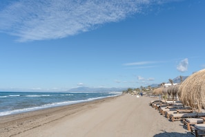 Una spiaggia con una fila di lettini di legno e ombrelloni di paglia lungo la battigia.