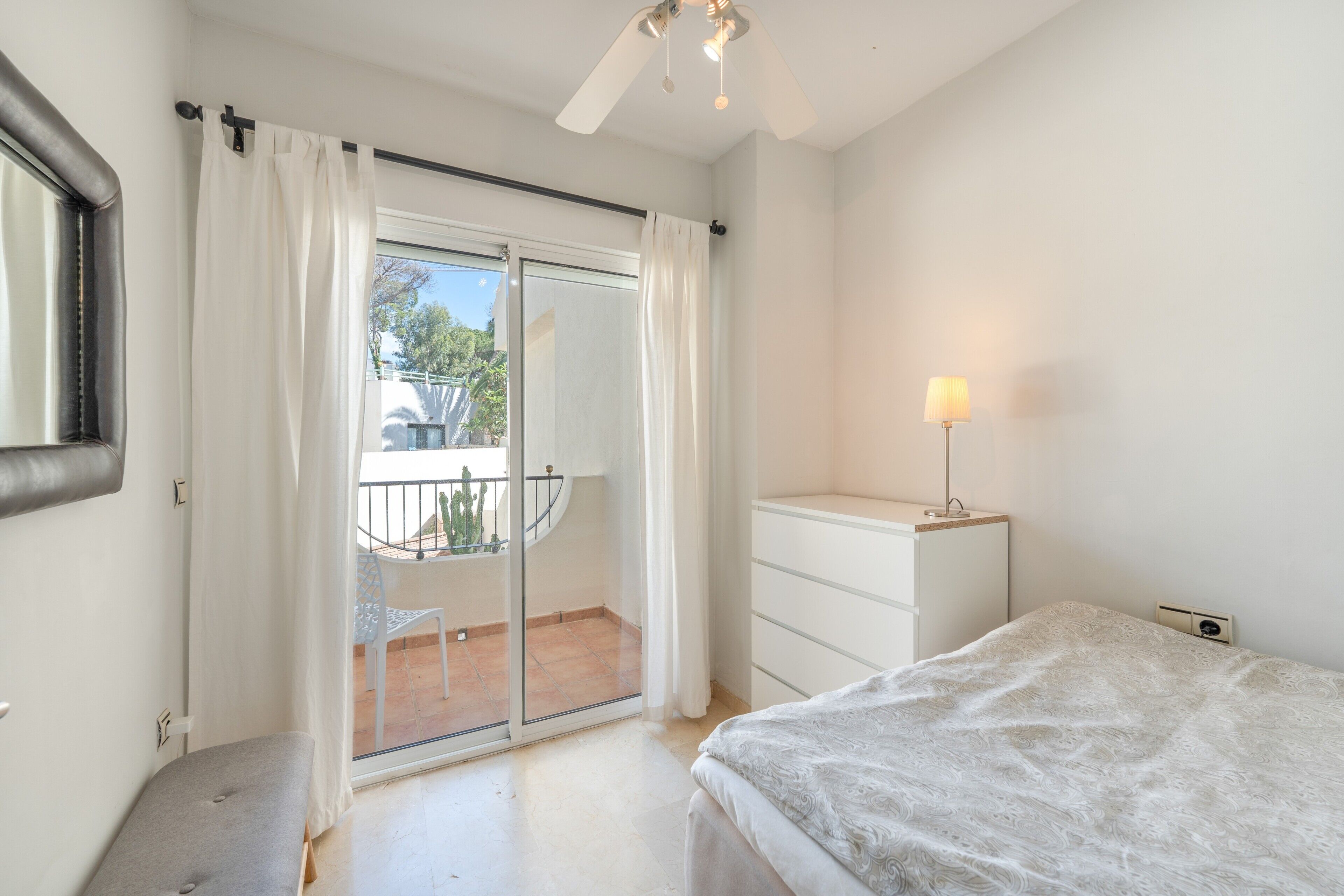 Une chambre avec un lit, une table de chevet, une lampe, une porte-fenêtre coulissante donnant sur un balcon et une chaise à l’extérieur.