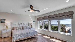 A bedroom with a bed, nightstands, a ceiling fan, and large windows with a view of the ocean. - Salt Therapy N - Coastal escape w/ beach access (St Augustine)