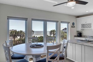 A dining area with a round table and chairs, large windows with a view of palm trees and buildings, and a kitchen with white cabinets and a countertop. - Salt Therapy - Elevated house w/ beach access (St Augustine)