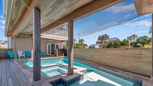 Una piscina con terraza de madera, zona cubierta y vistas del barrio.
