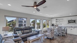 A spacious living room with a leather sofa, a coffee table, and a dining area with white chairs. - Salt Therapy S - Stylish retreat w/ beach & pool (St Augustine)
