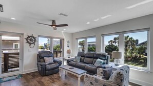 A spacious living room with leather sofas, a coffee table, and a view of the outdoors through large windows. - Salt Therapy S - Stylish retreat w/ beach & pool (St Augustine)