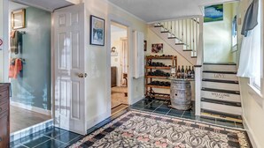 Un pasillo con un tapete estampado, un mueble para vinos y una escalera decorada con letreros que dicen 'LOVE' y 'WELCOME'.