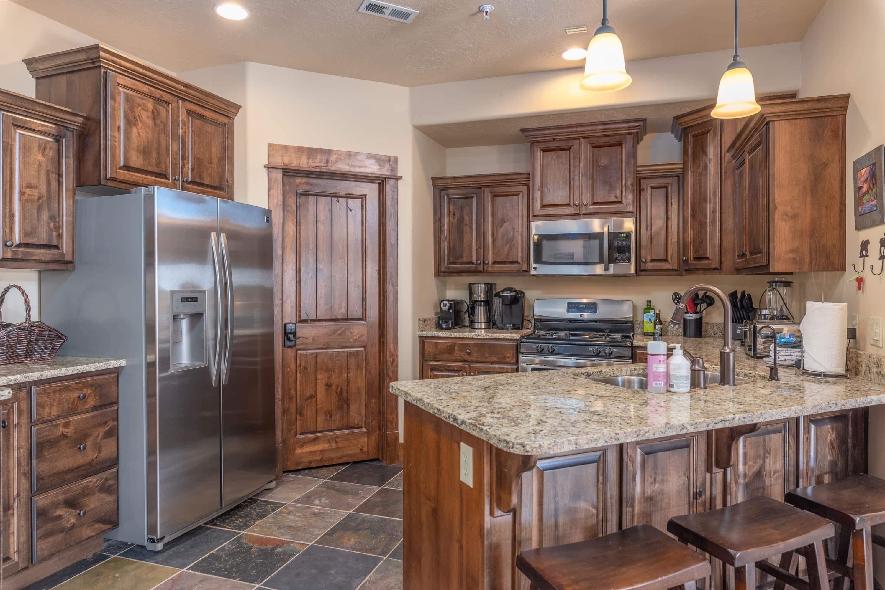 A kitchen with wooden cabinets, a stainless steel refrigerator, a microwave, and a granite countertop.
