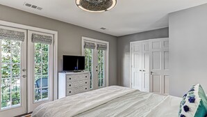 A bedroom with a bed, dresser, television, and large windows.