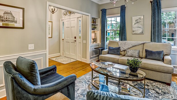 A living room with a sofa, armchair, and coffee table, a chandelier, and a door leading to another room.