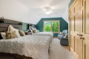 A bedroom with two beds, a nightstand, a dresser, a ceiling fan, and a window with a view of greenery.