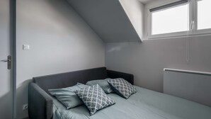 A bedroom with a sloped ceiling, a bed with two patterned pillows, a radiator, and a window with blinds.