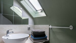 A bathroom with a white sink, a towel rack with folded towels, and a skylight above the mirror.
