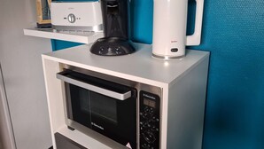 A kitchen area with a microwave, a coffee maker, and a kettle on a white countertop.