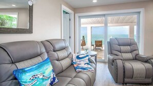 A room with a sofa and a recliner facing a large glass door leading to a balcony with a view of the ocean. - Dolfan Oceanfront Cottage Direct oceanfront with 50 ft of dockage and jacuzzi and kayaks 4 bed 2 bath home (Marathon)